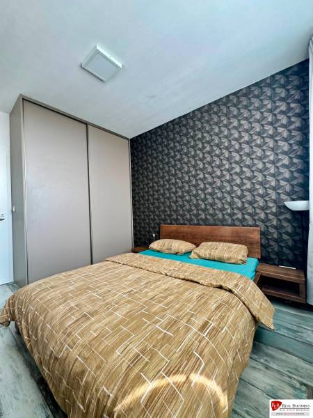 Ložnice v 2-pokojovém bytě s postelí a vzorovanou tapetou, podlaha s dřevěným dekorem.