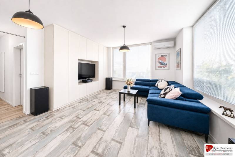 Obývací pokoj v 2-pokojovém bytě s modrou pohovkou a podlahou s dřevěným dekorem.