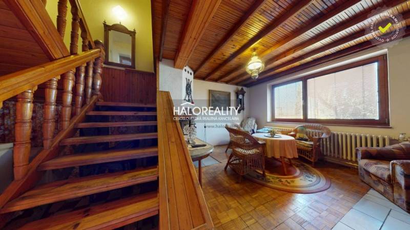 Interiér rodinného domu se schodištěm, podlahou s dřevěným dekorem a ratanovým nábytkem.