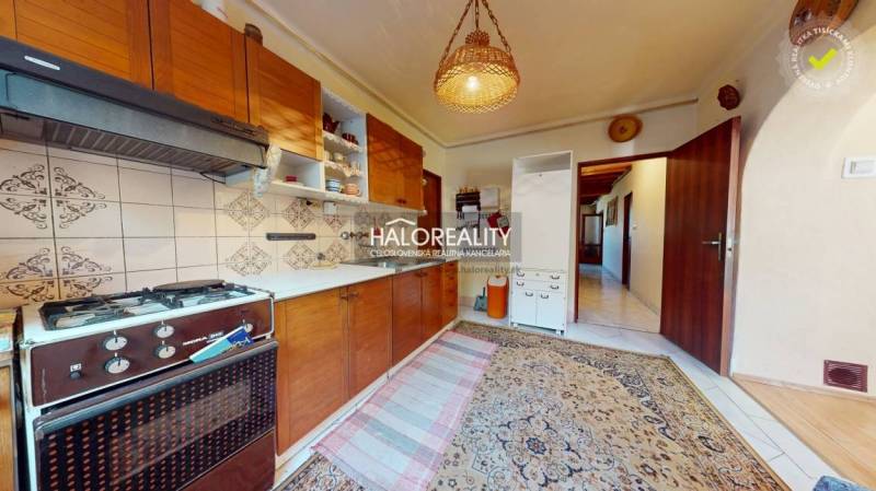 Kuchyně v rodinném domě s kobercem, plynovým sporákem a dřevěnými skříňkami.