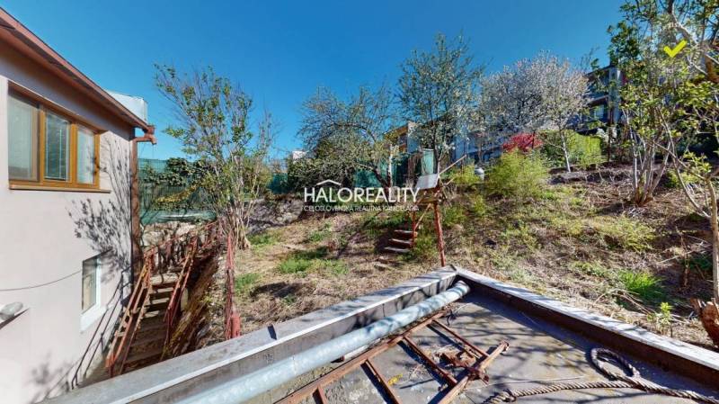 Rodinný dům v Rimavské Sobotě, vedle svažité zahrady se stromy.