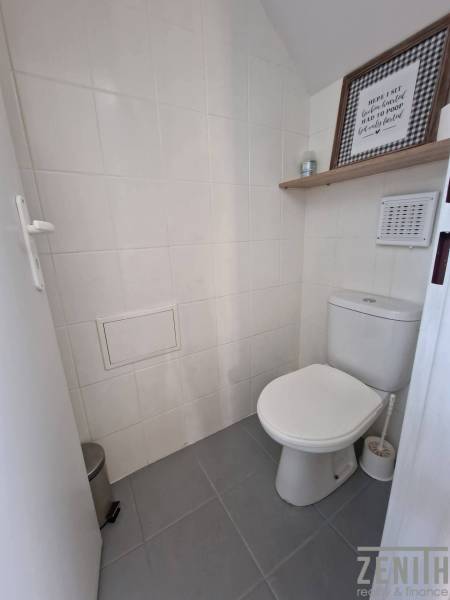 Toaleta s bílými dlaždicemi a dekorativní poličkou v obchodních prostorách.