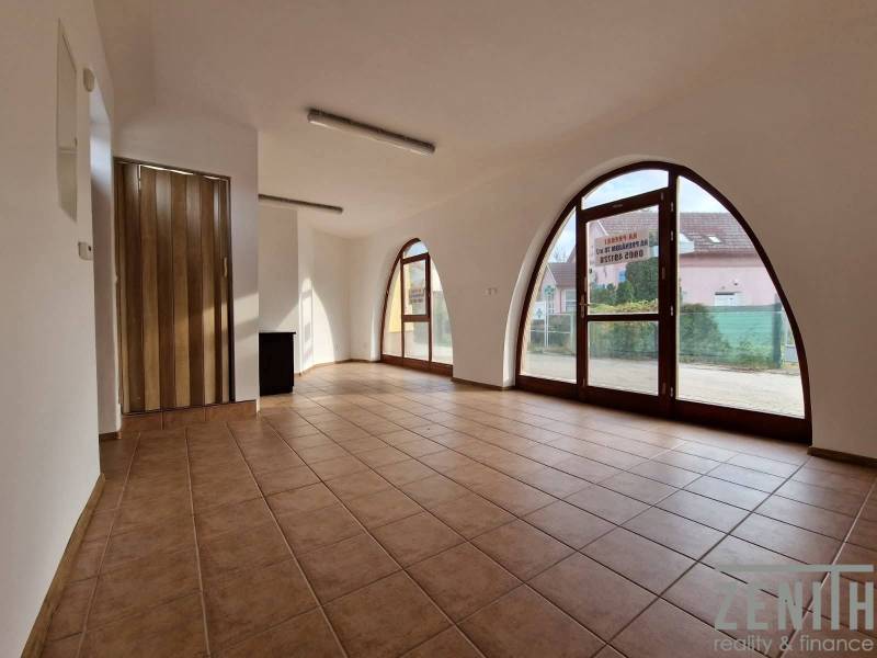 Interiér obchodních prostor s velkými obloukovými okny, dlažba a dřevěné dveře.