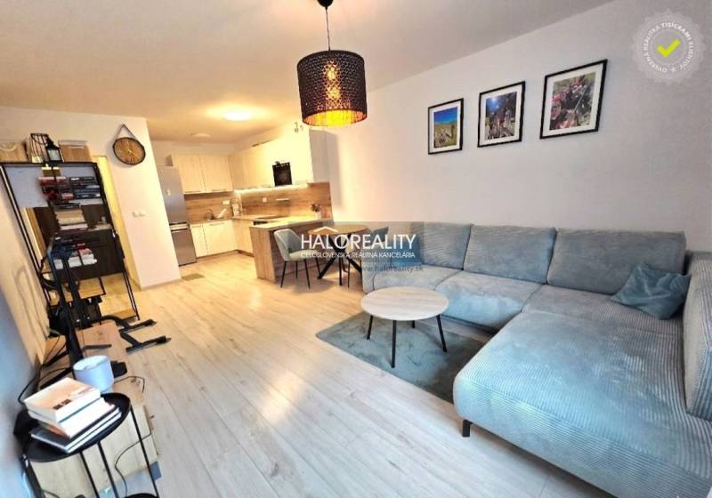 Obývací pokoj s rohovou sedačkou, kuchyní a podlahou s dřevěným dekorem v 2-pokojovém bytě.