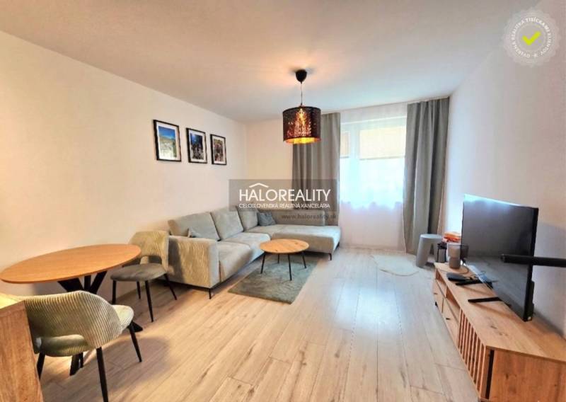 Světlý obývací pokoj v 2-pokojovém bytě s komfortní sedačkou a podlahou s dřevěným dekorem.