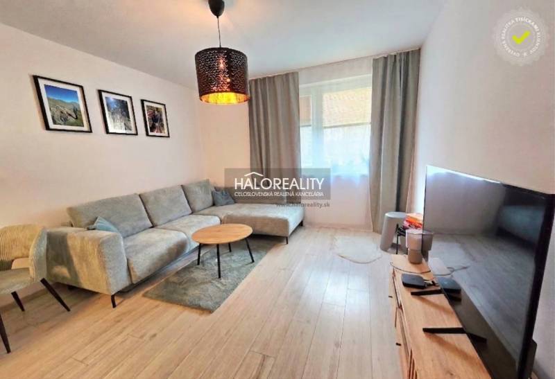 Obývací pokoj v dvoupokojovém bytě s podlahou s dřevěným dekorem a pohodlnou sedací soupravou.