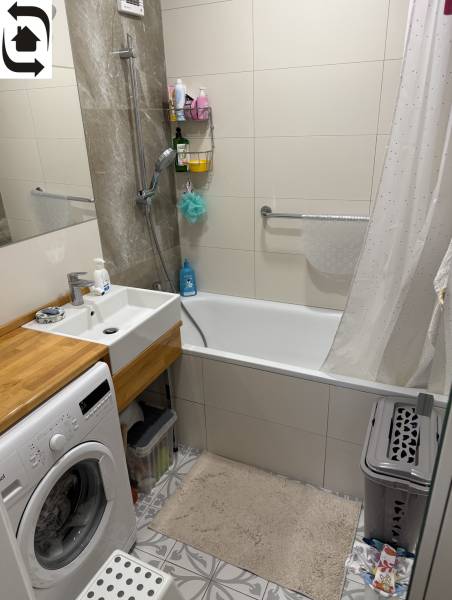 Koupelna se sprchovací vanou a pračkou ve 4-pokojovém bytě s elegantními dlaždicemi.