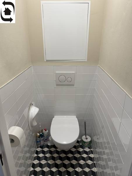 Toaleta ve 4-pokojovém bytě s geometrickou dlažbou a bílými obklady.