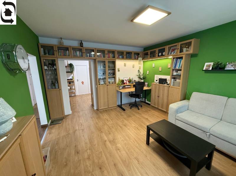 Obývací pokoj ve 4pokojovém bytě, s podlahou s dřevěným dekorem a knihovnou.
