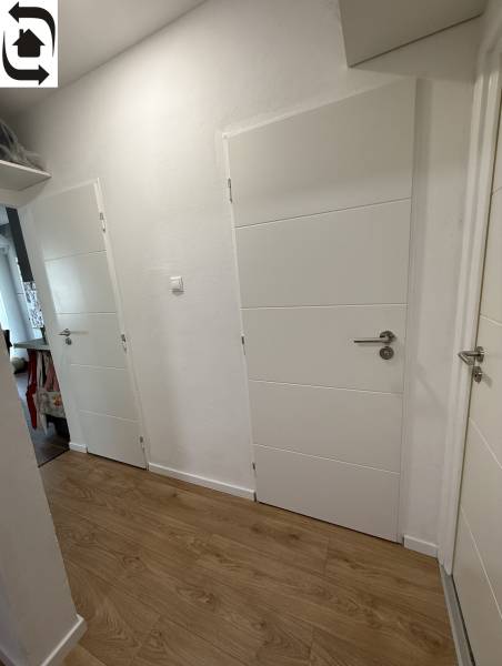 Chodba ve 4-pokojovém bytě s bílými dveřmi a podlahou s dřevěným dekorem.