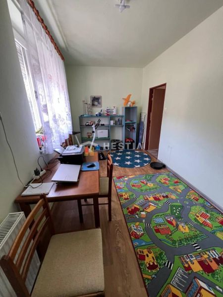 Dětský pokoj s kobercem ve tvaru cesty, pracovním stolem a policovým regálem.