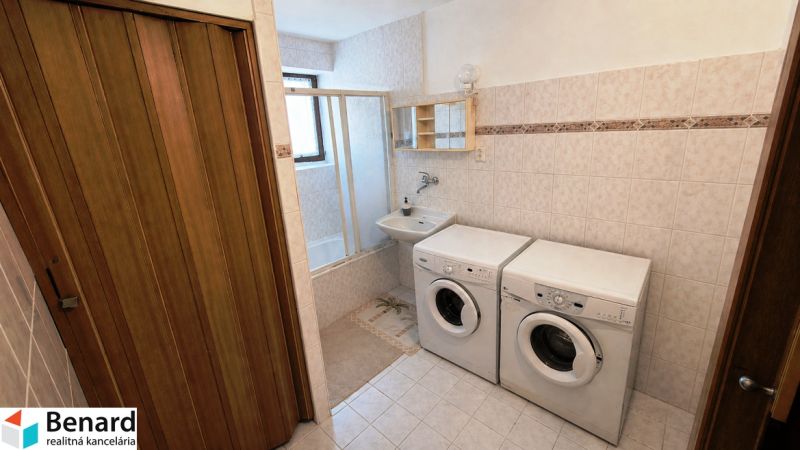 Koupelna v rodinném domě s pračkou, sušičkou a vanou na světlé dlažbě.