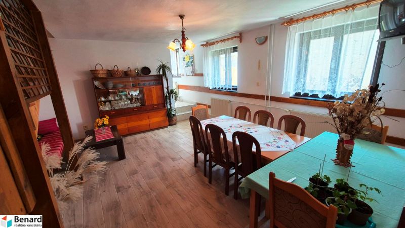 Interiér rodinného domu s jídelním stolem, příborníkem a podlahou s dřevěným dekorem.