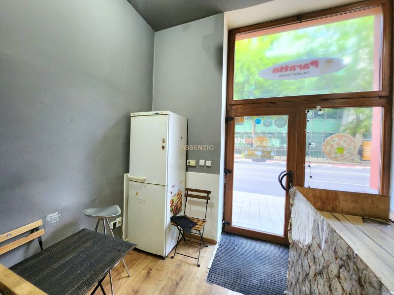 Gastro prostory s podlahou s dřevěným dekorem, lednice u stolu a vstupní dveře.