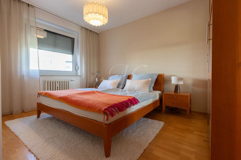 Ložnice s manželskou postelí, nočním stolkem a podlahou s dřevěným dekorem ve 4pokojovém bytě.