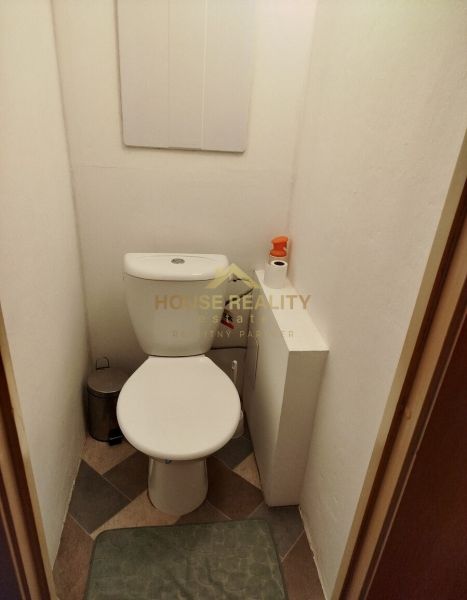 Toaleta v 1-pokojovém bytě s dlažbou a hygienickým příslušenstvím.