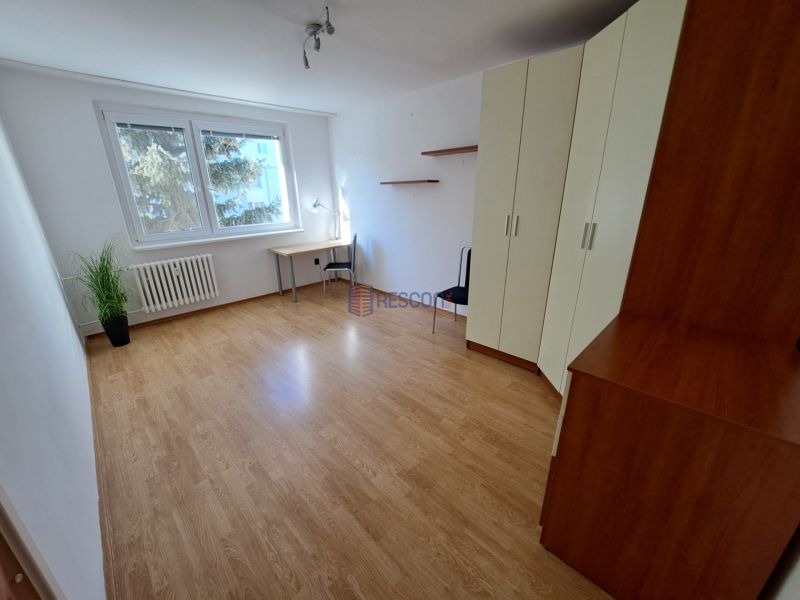 Pokoj s podlahou s dřevěným dekorem, velkými okny, skříní a psacím stolem.