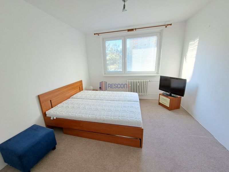 Světlá ložnice v 2pokojovém bytě s manželskou postelí a televizorem.