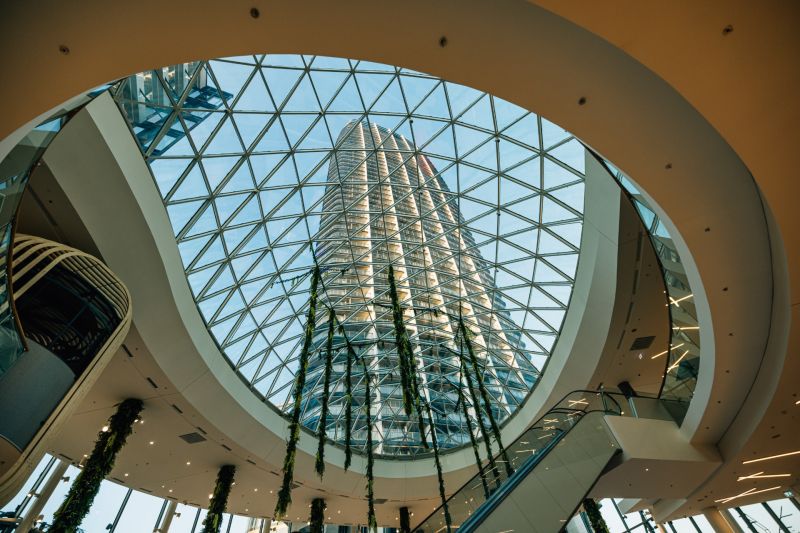 Prostorné atrium se skleněnou střechou a vysokou budovou v pozadí.