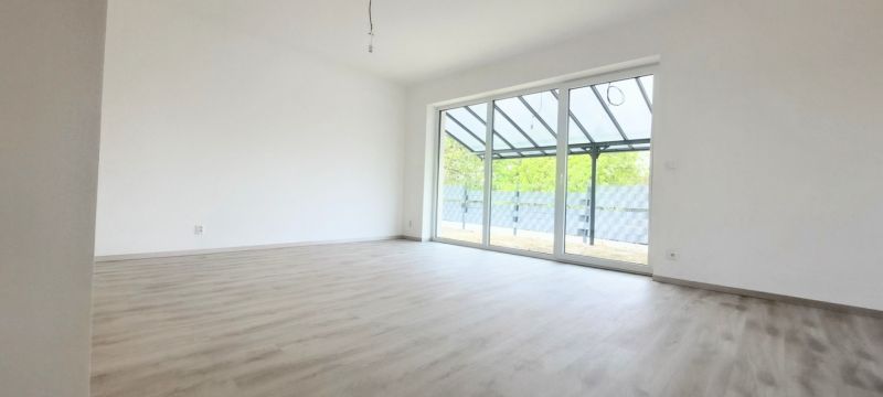 Prostorná místnost v rodinném domě s podlahou s dřevěným dekorem a velkým prosklením.