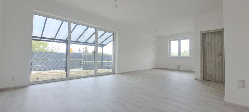 Prostorný interiér rodinného domu s velkými okny a podlahou s dřevěným dekorem.