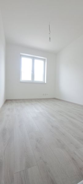 Pokoj s bílými stěnami, podlahou s dřevěným dekorem a oknem v rodinném domě.