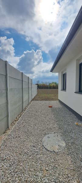 Rodinný dům v Selicích s betonovým plotem a štěrkovou dlažbou na dvoře.