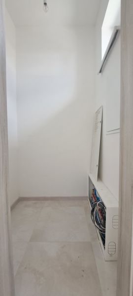 Úzká místnost s rozvaděčem v rodinném domě, světlé dlaždice, neutrální stěny.