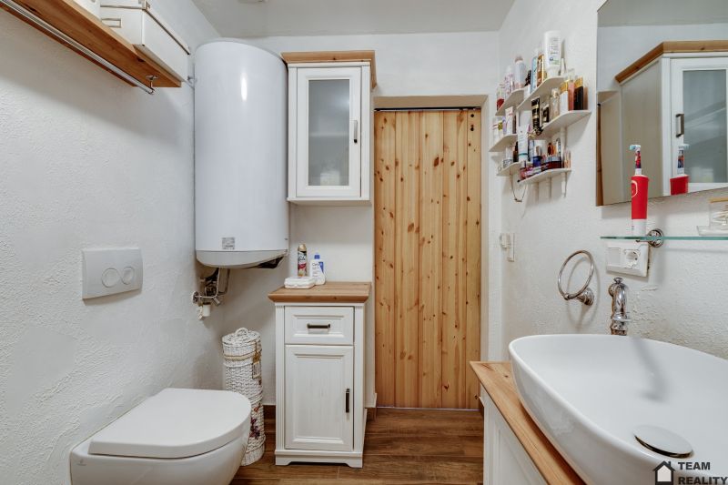 Koupelna v rodinném domě s WC, umyvadlem a skříněmi, podlaha s dřevěným dekorem.