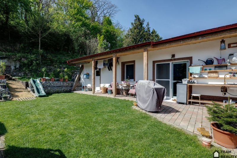 Rodinný dům v Potzneusiedlu s terasou, zelení a dětskou skluzavkou, obklopený přírodou.