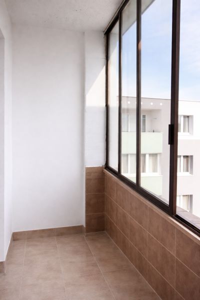 Zasklený balkon ve 4-pokojovém bytě se světlou dlažbou a výhledem na bytovku.