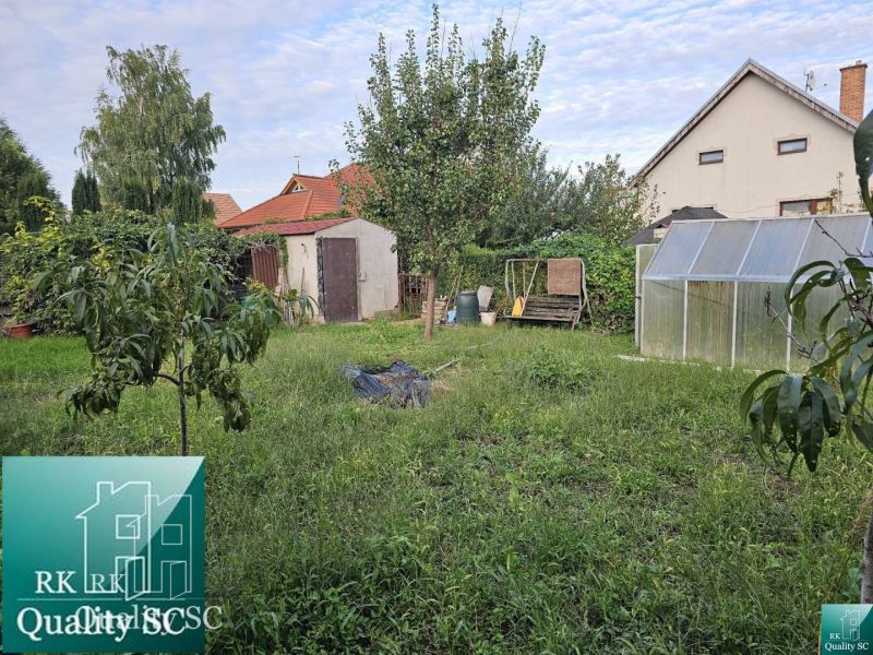 Zahrada rodinného domu v obci Tureň s trávníkem, skleníkem a stromy.