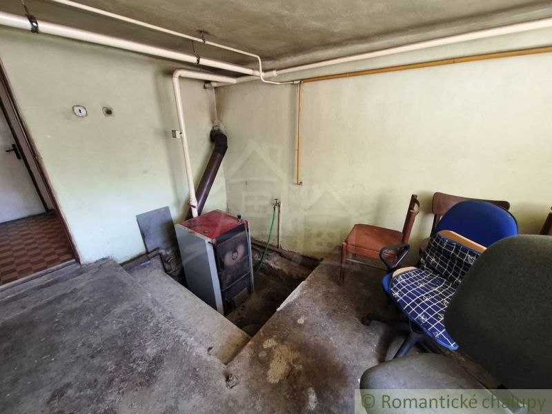 Stará kotelna v rodinném domě s kancelářskými židlemi a potrubím na stěně.