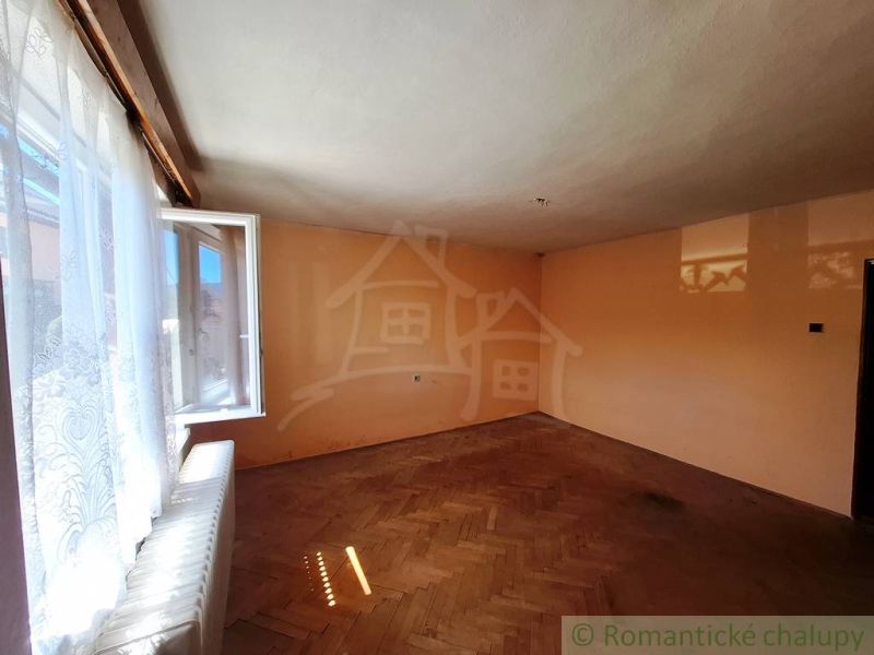Otevřená místnost s podlahou s dřevěným dekorem, okno s bílými závěsy.