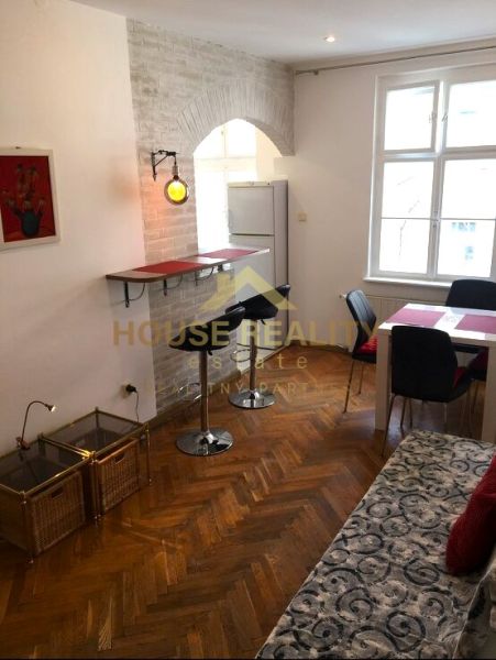 Obývací pokoj dvoupokojového bytu s podlahou s dřevěným dekorem, barem a jídelním stolem.