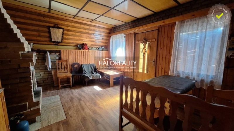 Interiér chaty s podlahou s dřevěným dekorem a zděným krbem, útulná atmosféra.