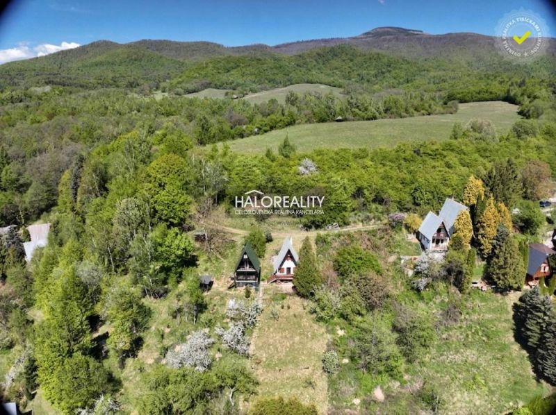 Chata v Chyžném obklopená lesy a zelenými loukami pod horskou panorámou.