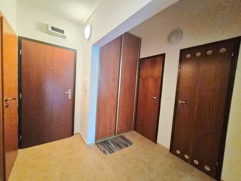 Předsíň v 2-pokojovém bytě s dřevěnými dveřmi a dlažbou na podlaze.