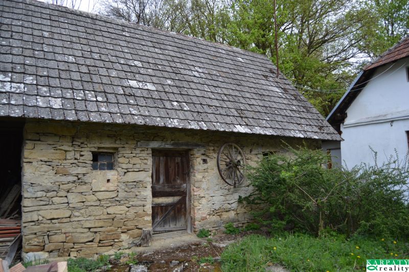 Kamenná stodola u rodinného domu v Bukovci s dřevěnými dveřmi a střešními taškami.