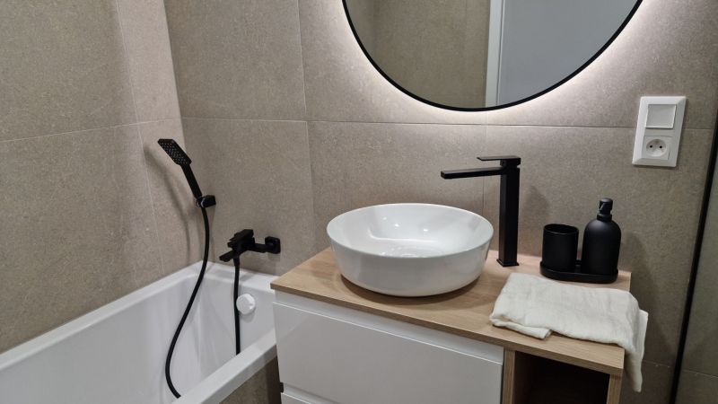 Koupelna v 3-pokojovém bytě s kruhovým zrcadlem a moderními bateriemi.