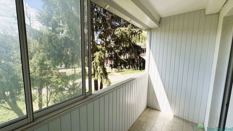 Zasklený balkon ve 4-pokojovém bytě s výhledem na stromy, bílá dřevěná stěna.