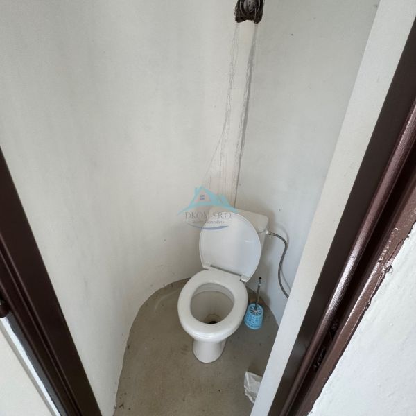 Jednoduchá toaleta v chatě se stěnou bez obkladu a plastovým WC.