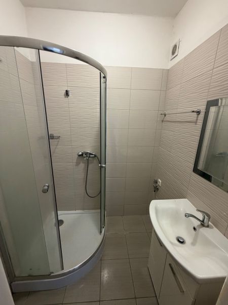Koupelna s rohovým sprchovým koutem a umyvadlem v 1-pokojovém bytě.