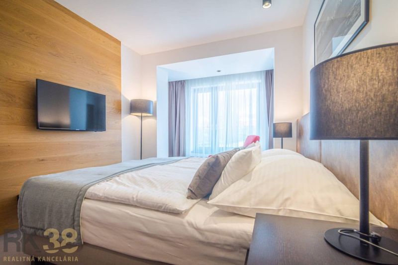 Rekreační apartmán s pohodlnou postelí, podlahou s dřevěným dekorem a velkými okny.