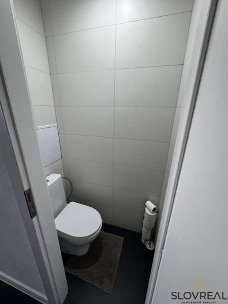 Toaleta v 3-pokojovém bytě s minimalistickými šedými obklady a tmavou podlahou.