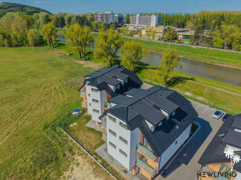 Bytový dům s černou střechou u řeky na Moravanské ulici v Bance.
