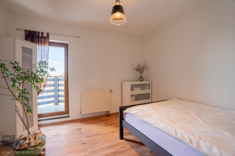 Světlá ložnice ve 4-pokojovém bytě s podlahou s dřevěným dekorem, rostlinou a balkonem.