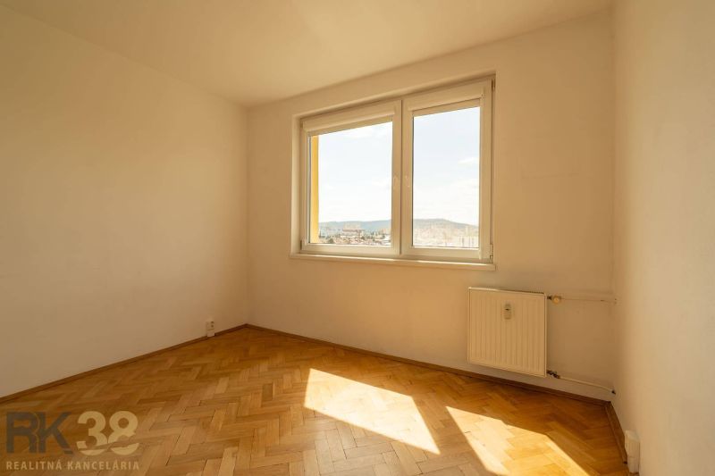 Pokoj s oknem, radiátorem a podlahou s dřevěným dekorem ve 4-pokojovém bytě.