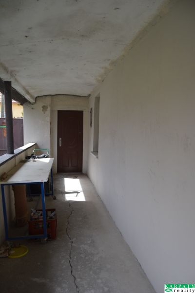 Chodba s bílými stěnami, praskliny na podlaze, stůl, dveře v rodinném domě.