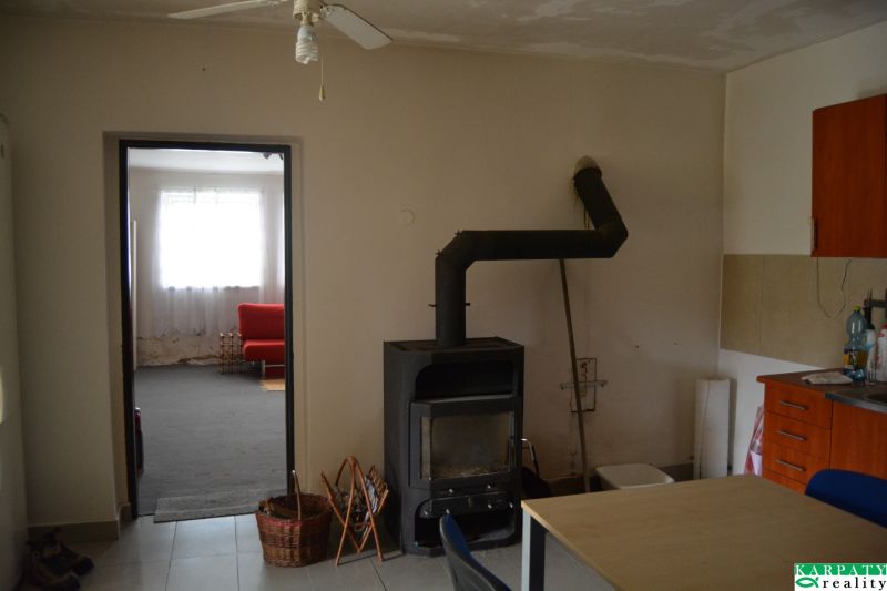 Interiér rodinného domu s krbem, ventilátorem a červenou sedačkou v pozadí.